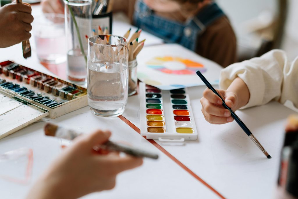 pexels-photo-7898415-7898415 Children's hands holding paintbrushes while painting with watercolors during a creative art session.